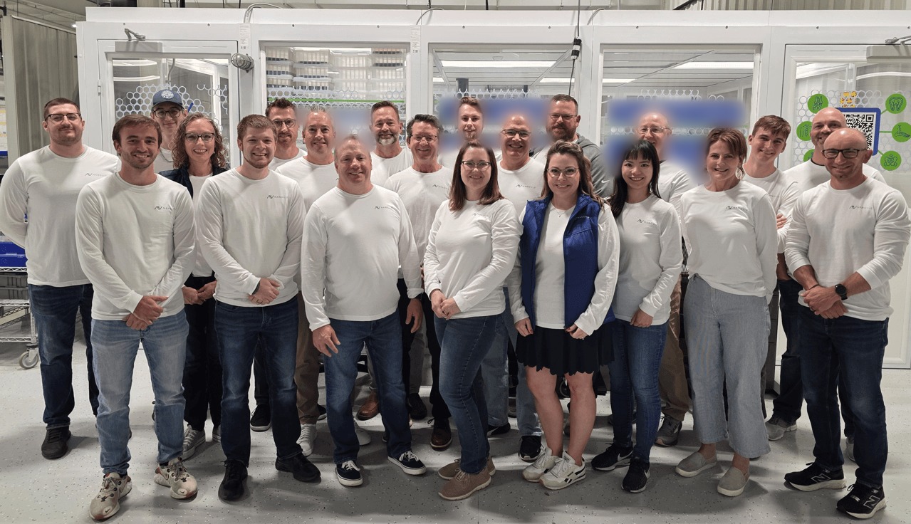 The Nanovis team standing together in the company facility, wearing matching white Nanovis shirts